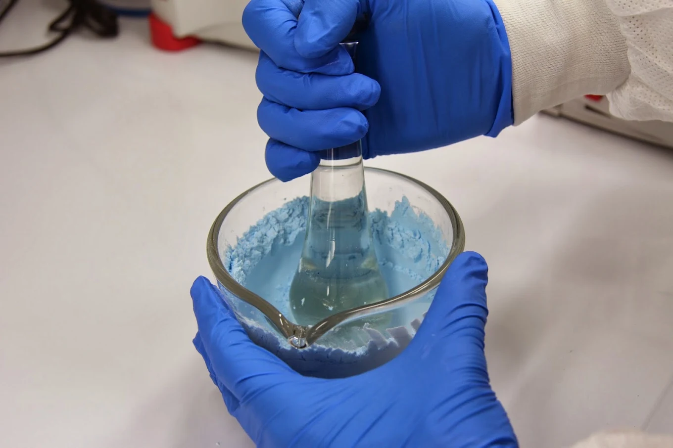 Hands in blue gloves grinding medication with a mortar and pestle